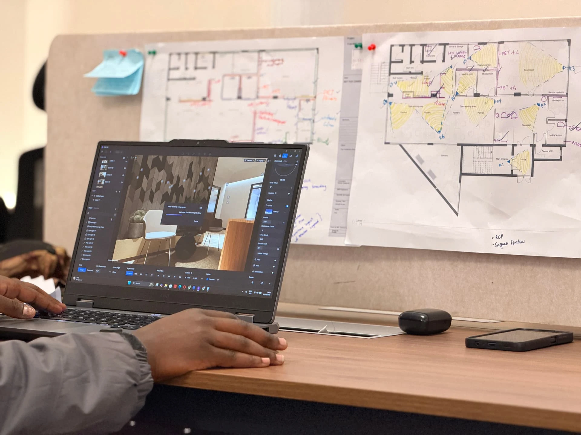 Designer rendering an interior scene on a laptop beside marked-up floor plans